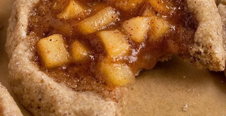 Chewy vegan apple pie cookies on a baking sheet with cinnamon and apples