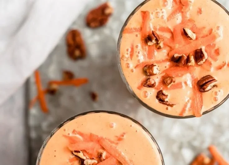 A vibrant Orange Carrot Smoothie with ginger in a glass, garnished with fresh carrots